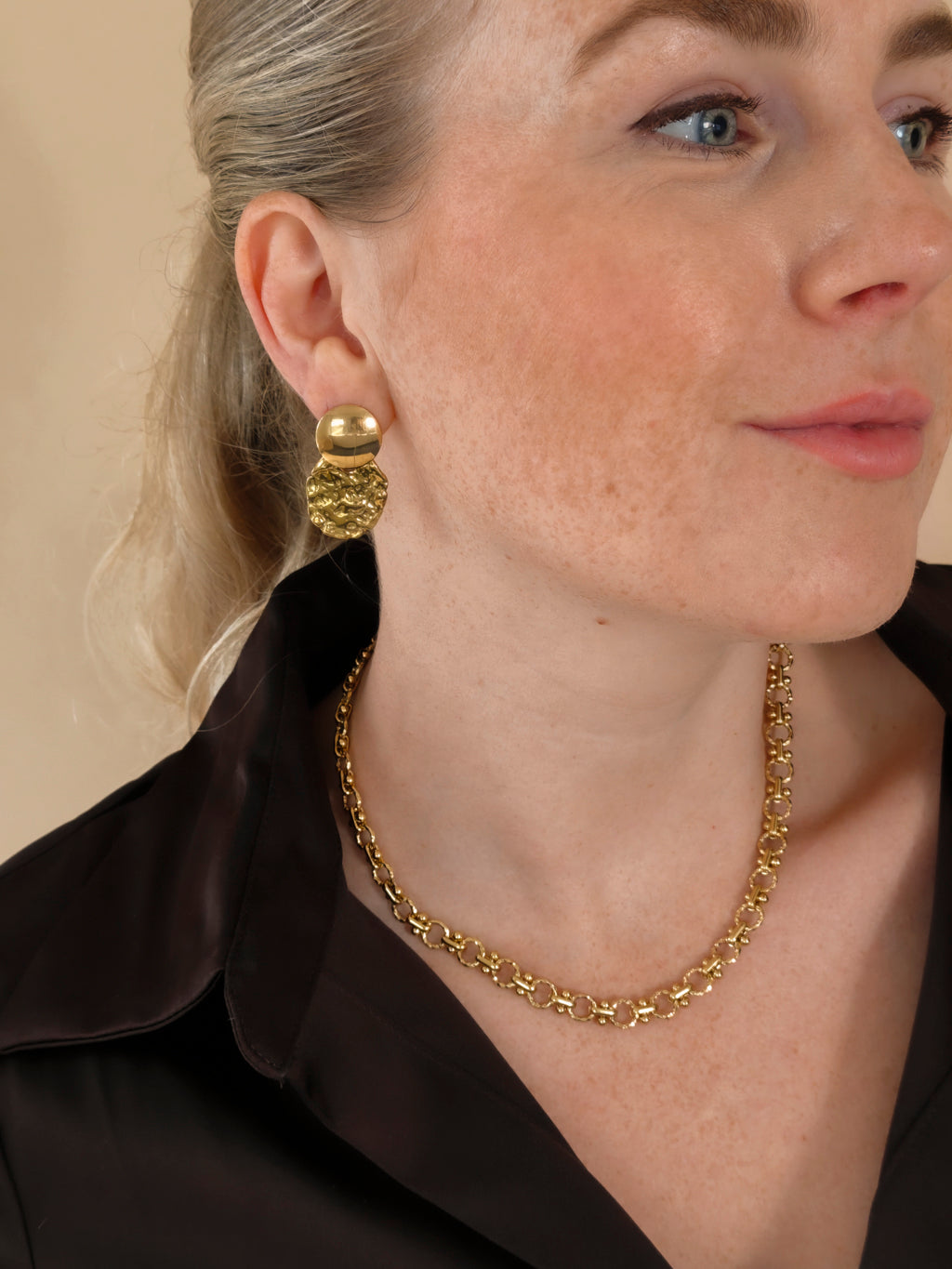 Solene gouden oorbellen gedragen met een donkere blouse en Lace ketting