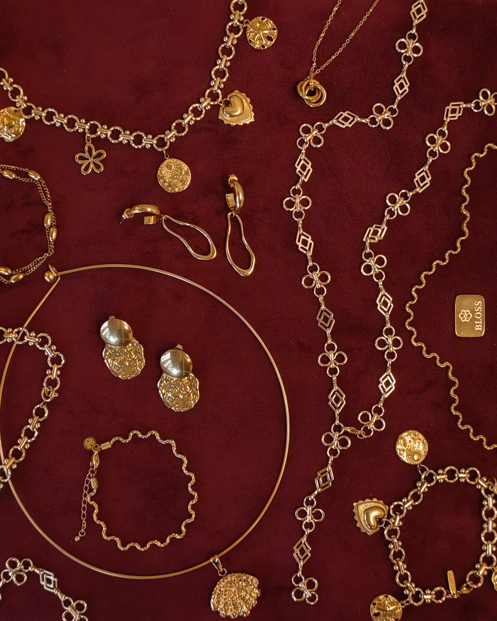 Gouden BLOSS Essentials met Solene en Ovelle oorbellen en Odine sieraden op bordeauxrode stof