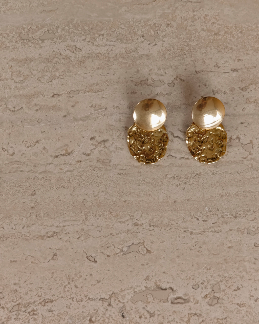 Gouden Solene oorbellen op een lichte stenen ondergrond
