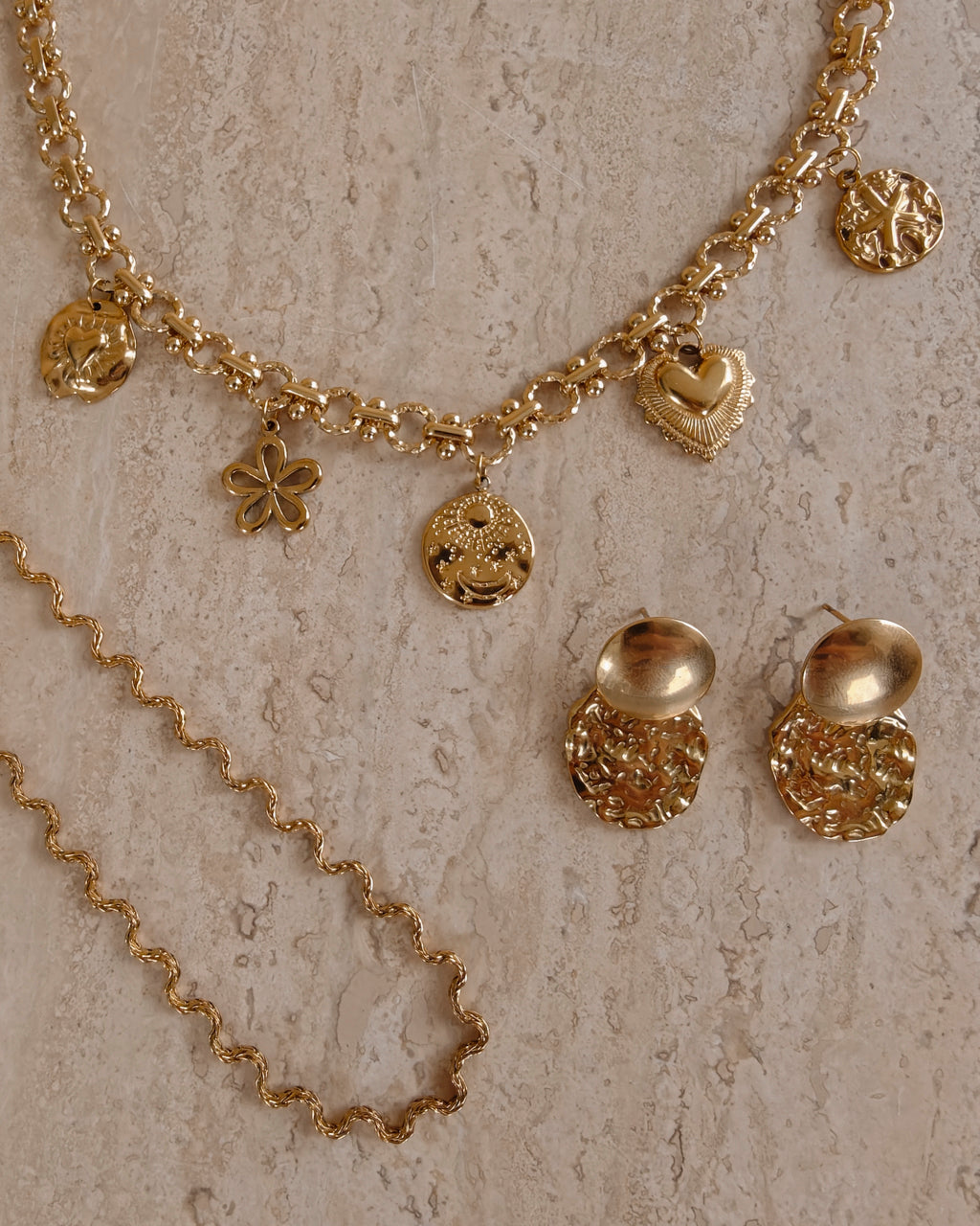 Gouden Coquette bedelketting en golvende Odine ketting naast gouden oorbellen