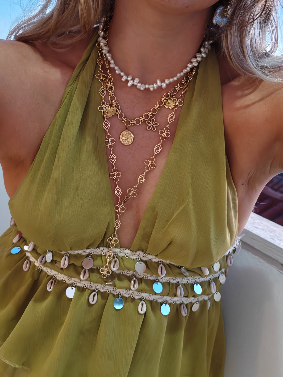 Gouden Coquette bedelketting en lange Fleurette Y-ketting gecombineerd met parels bij een groene outfit