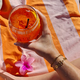 Odine Armband gecombineerd met andere gouden armbanden bij een oranje drankje