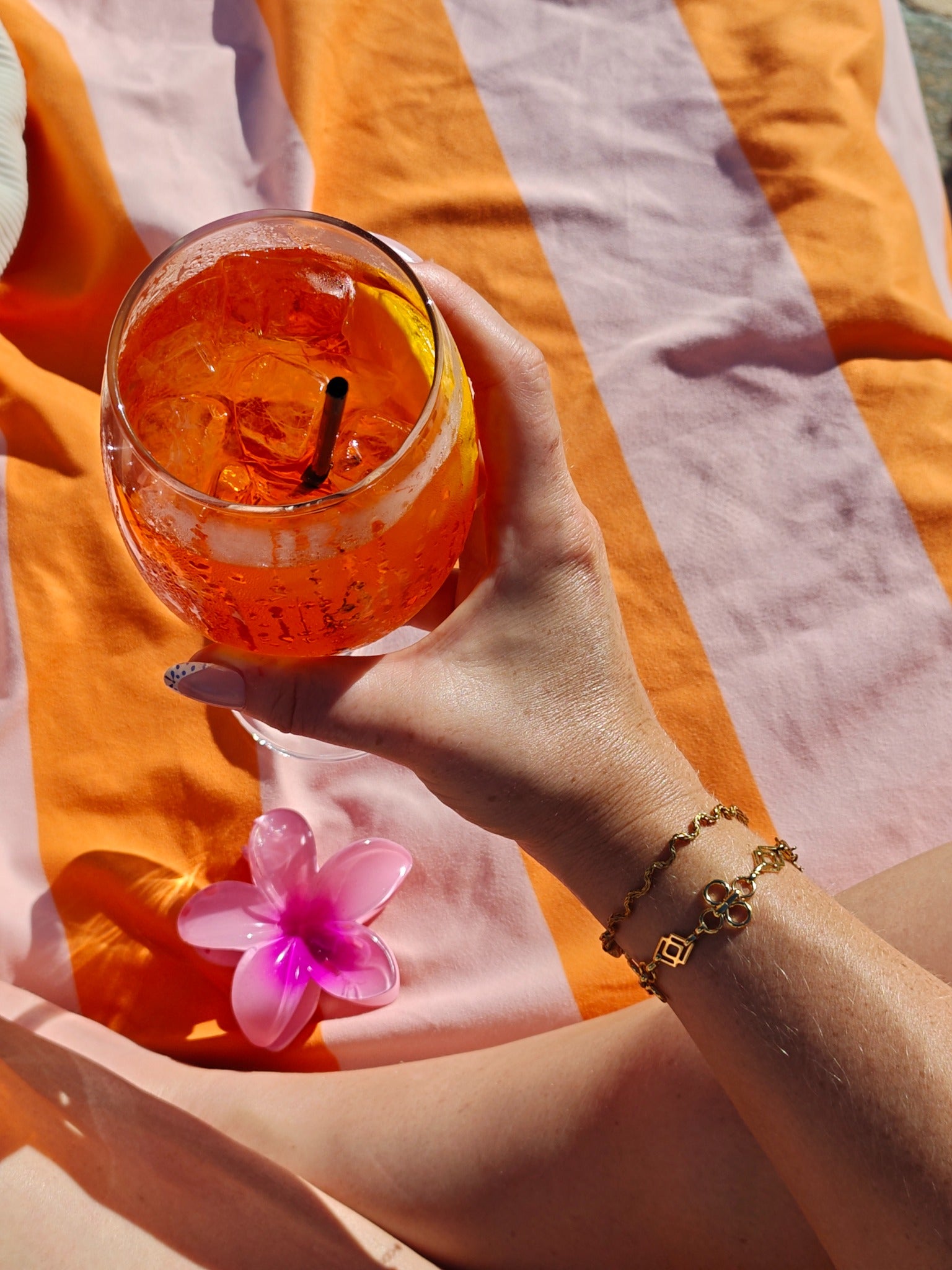 Odine Armband gecombineerd met andere gouden armbanden bij een oranje drankje